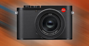 A black Leica camera with a textured body and a prominent lens is centered against a dynamic orange and blue blurred background. The brand's red logo is visible on the upper right corner of the camera body.