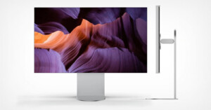 A sleek, modern computer monitor displays a vivid image of purple and orange rock formations. The side view shows the monitor's slim profile and minimalist stand design against a white background.