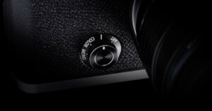 Close-up of a camera's mode dial, positioned at the corner of the device. The textured surface shows options for "Color" and "Mono" settings, with "ART" partially visible. The dial is shiny and metallic, contrasting with the dark camera body.