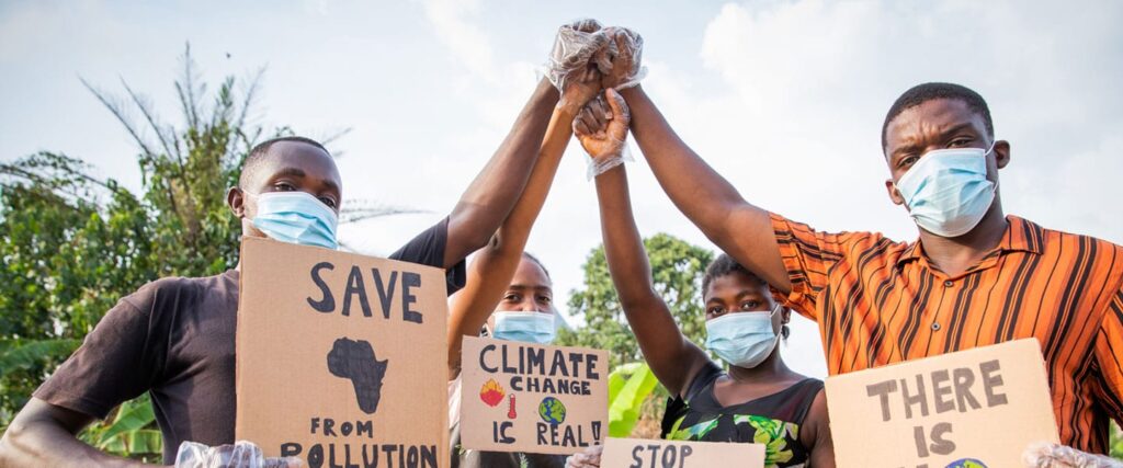 Individuals wearing masks holding signs about environmental conservation and climate change, raising their hands together in solidarity.