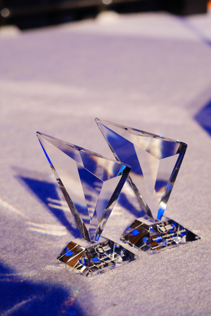 Two clear, triangular crystal awards displayed on a table with a blue cloth.