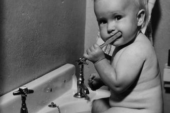 Adorable baby brushing teeth while sitti