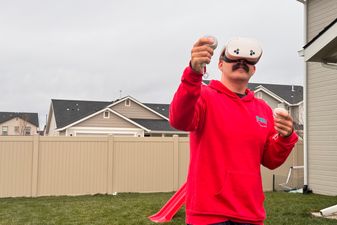 A man wearing a VR headset, holding two controllers, standing outside using the headset.