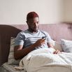 Man sitting at the bed after waking up and looking at his smartphone