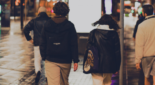 A group of three young people walk away from the camera on a rainy city street