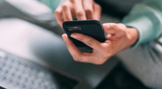 Close up of a woman's hands holding a phone with a laptop open