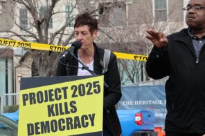 Two people on a podium with a board that reads "Project 2025 kills democracy"