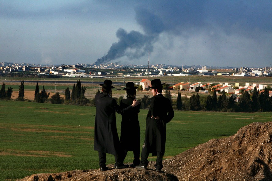 Três judeus ultraortodoxos contemplam coluna de fumaça que se aproxima de Gaza