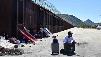 Um migrante espera com seus pertences ao lado do muro da fronteira EUA-México depois de entrar nos EUA vindo do México em Jacumba Hot Springs. — Foto: Frederic J. BROWN / AFP