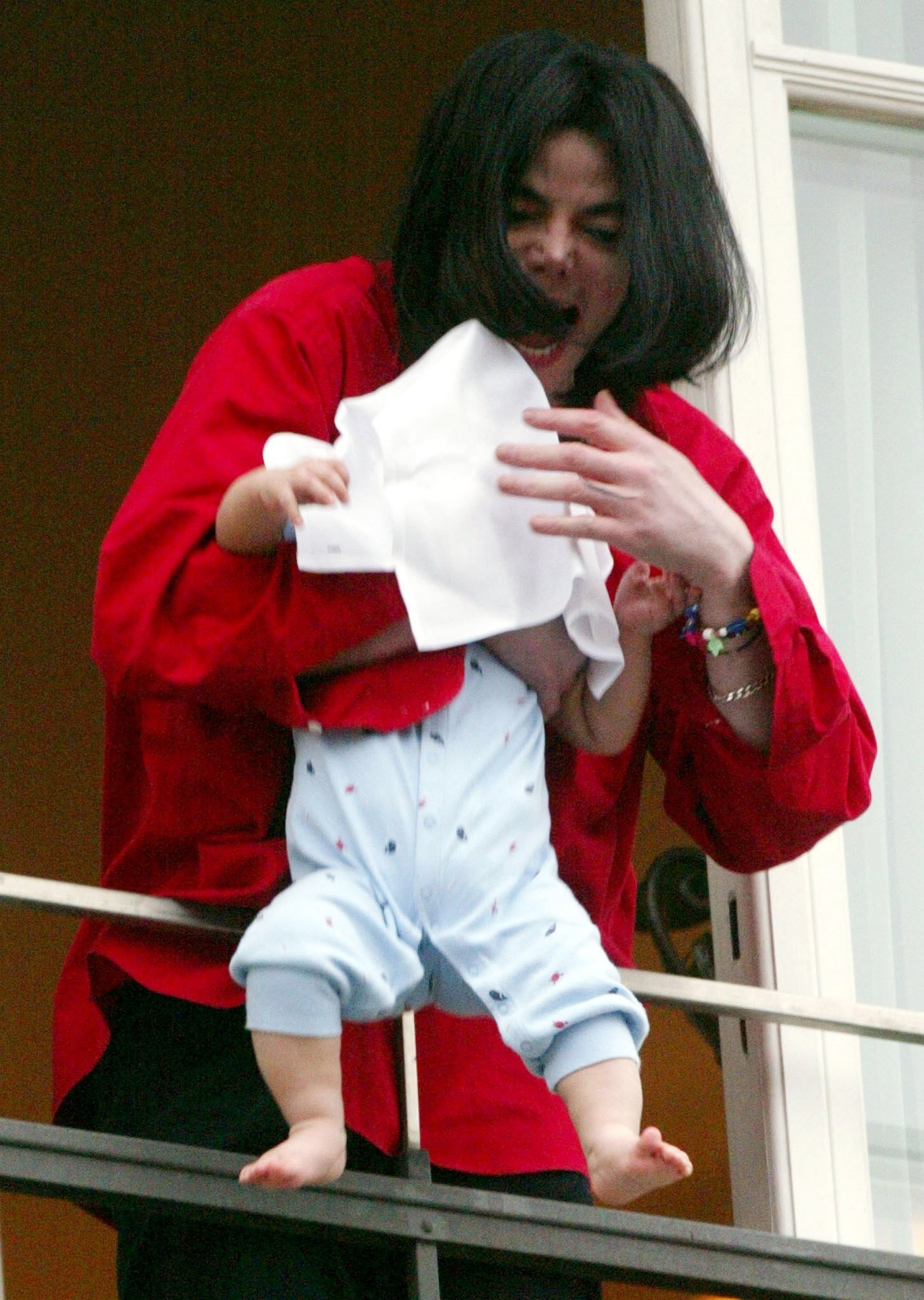 Michael Jackson balança o filho Bigi, em 2002, à beira de uma sacada de um hotel em Londres: criança foi apelidada por ele de Blanket ("cobertor", em inglês), já que ele protegia o rosto do bebê em aparições públicas — Foto: Tobias Schwarz