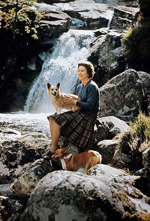 HM The Queen sitting on rocks beside a waterfall on the Garbh Allt burn with two corgis on the Estate at Balmoral Castle, Scotland during the Royal Family's annual summer holiday in September 1971. Part of a series of photographs taken for use during the Silver Wedding Celebrations in 1972.