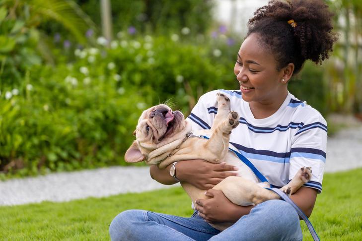 Young woman sitting in the grass holding her French Bulldog.