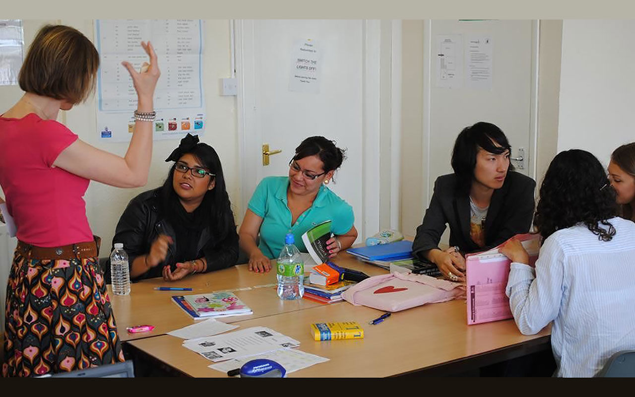 Adults sitting at a table with paper, pens, water botles, dictionary, and speaking with each other and a program facilitator