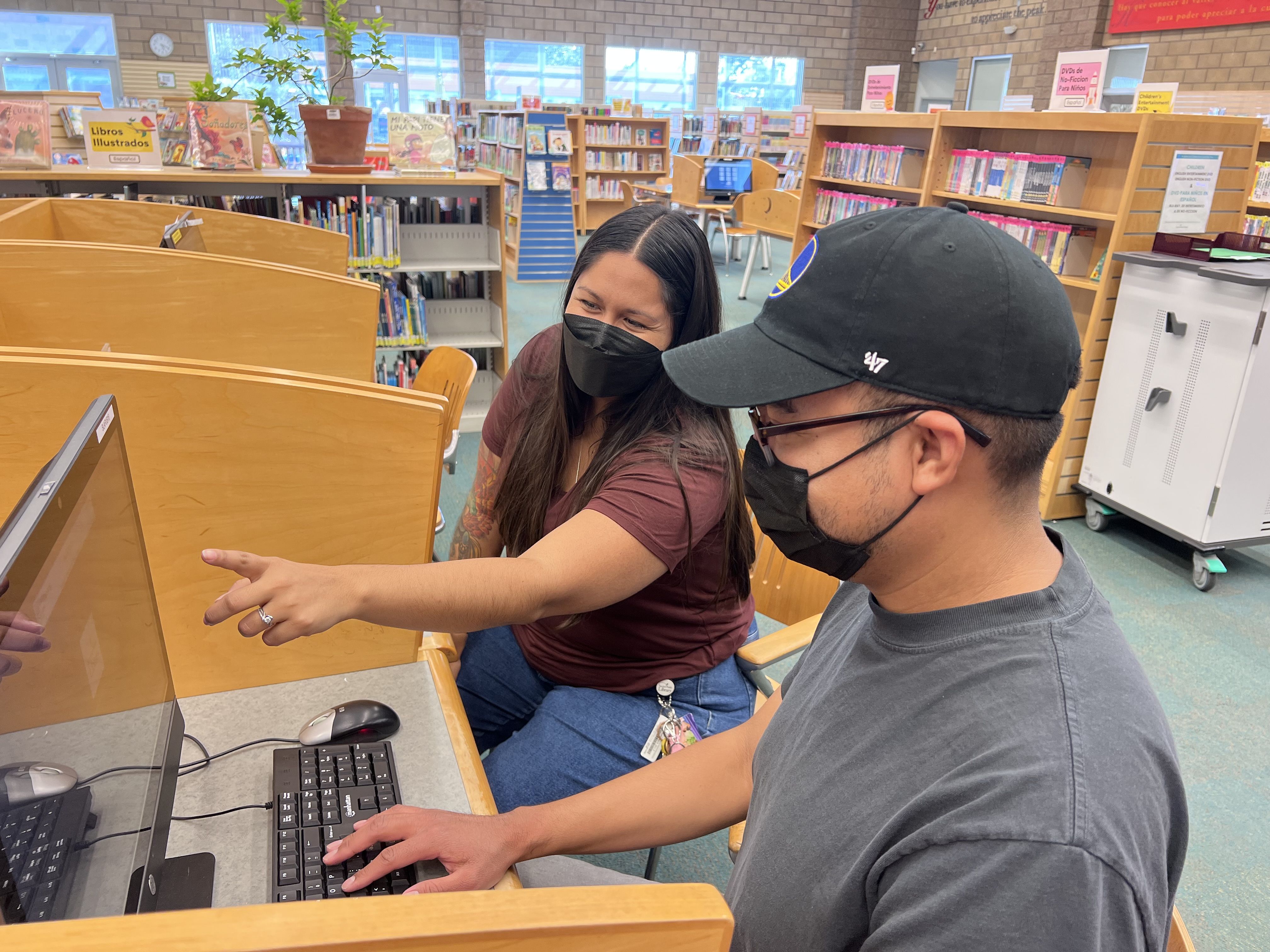 Two people sitting at a computer, one helping the other