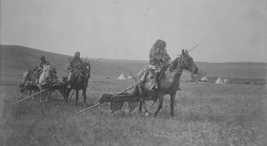 Atsina on horses with travois sledges behind them, tipis in background, Montana, Edward S. Curtis, Moving camp, 1908, photographic print (Library of Congress) 