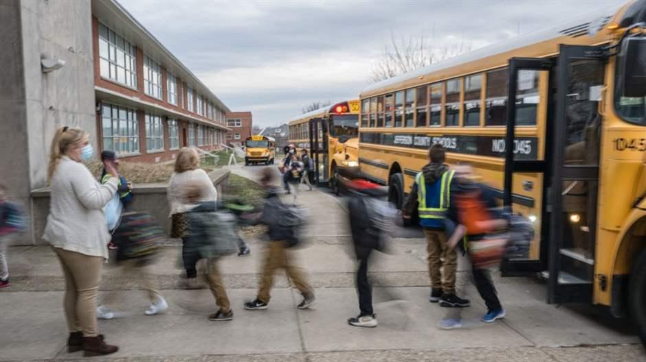 A teacher waves to her students as they get off the bus at an elementary school in Louisville, Ky., as they return to school following a COVID-19 outbreak in January 2022.