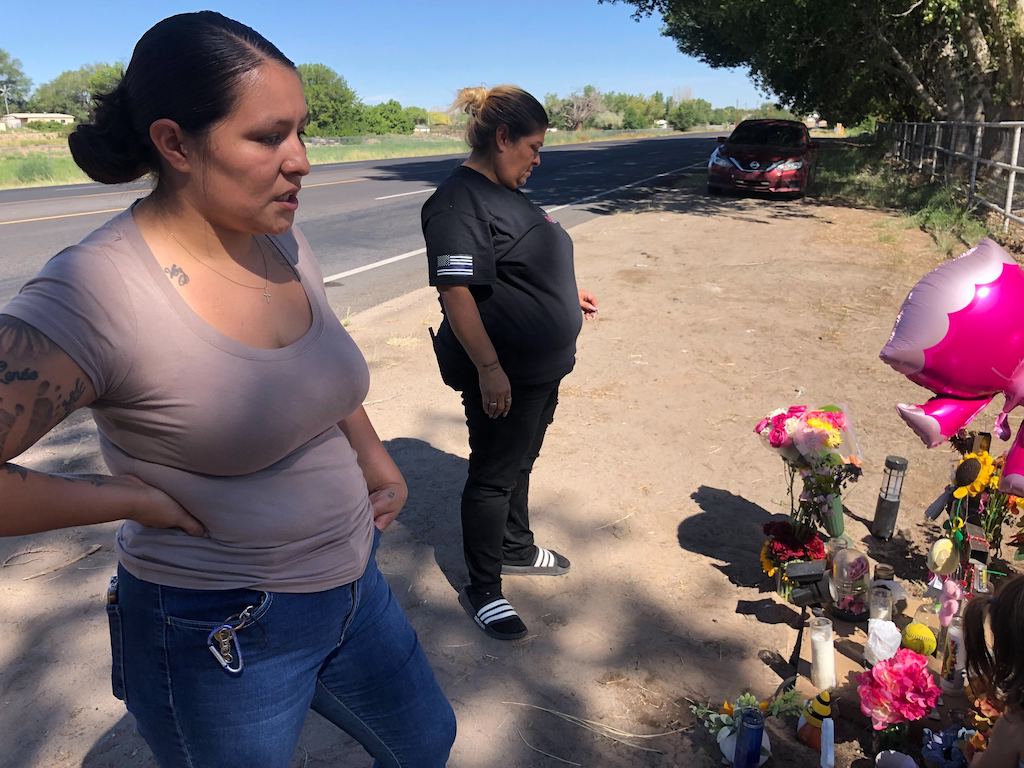 Two women stand at a roadside memorial.