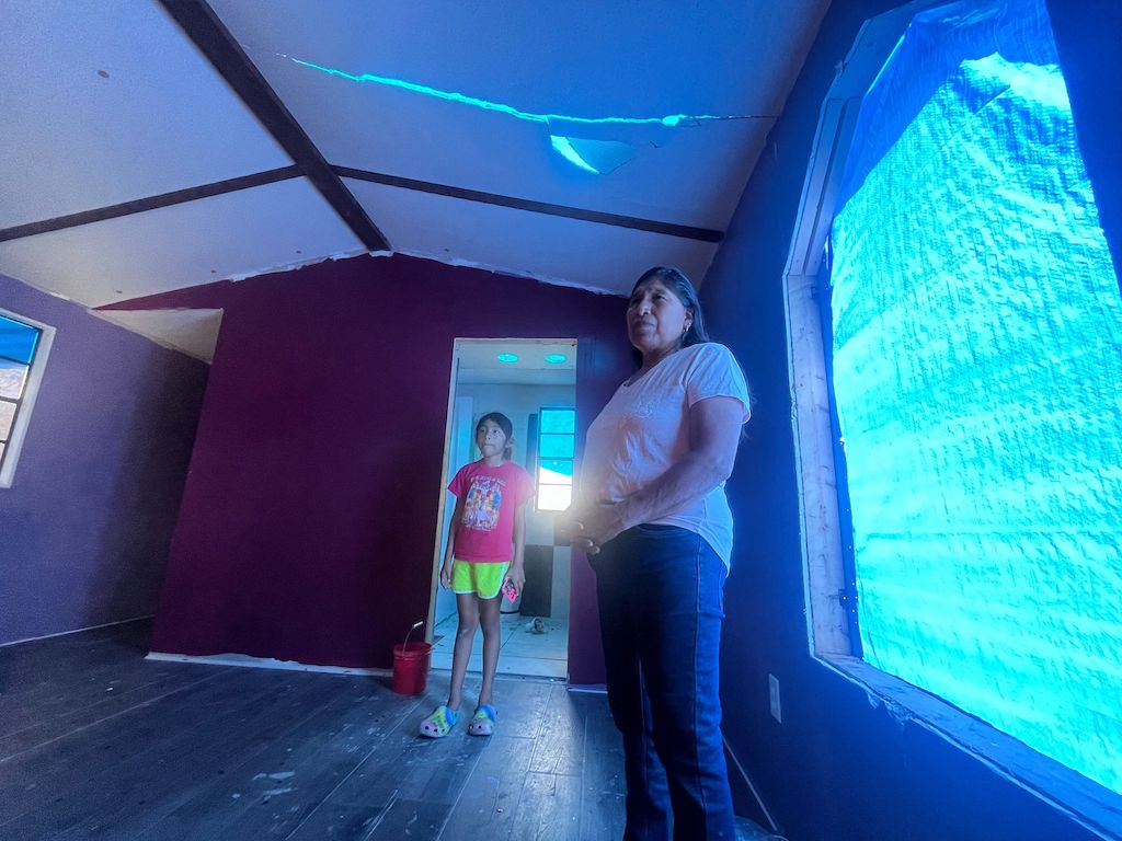 A woman and child stand in a storm-damaged mobile home.