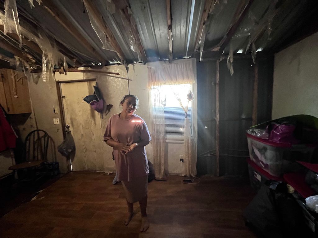 A woman stands in her storm-damaged home.