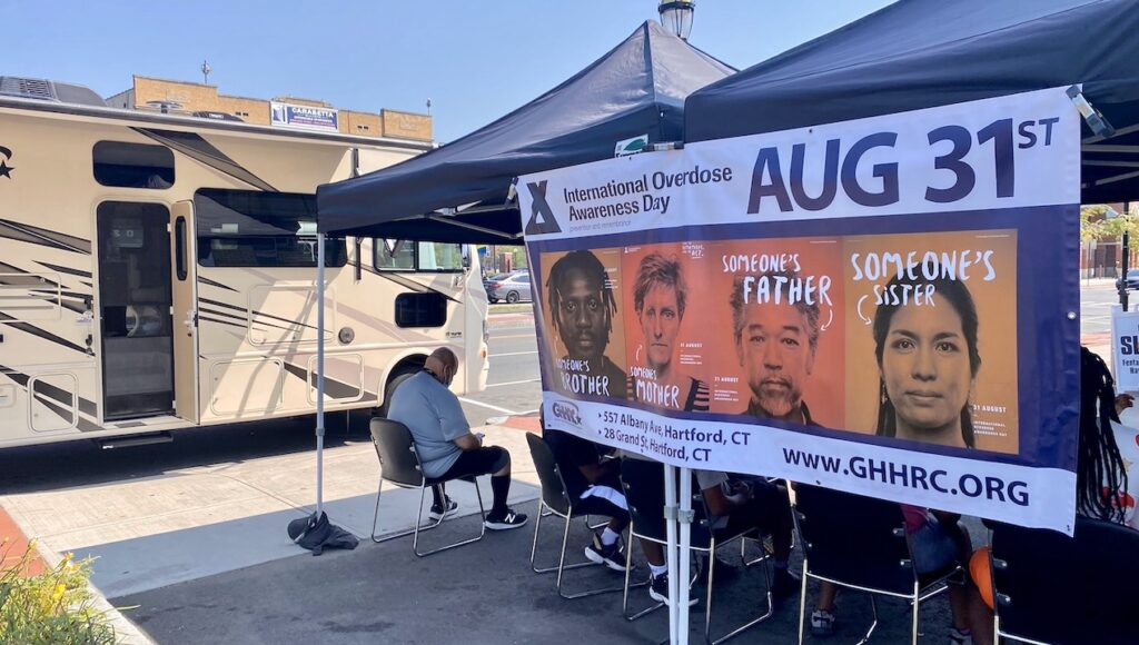 A man sits under a tent at an overdose awareness event.