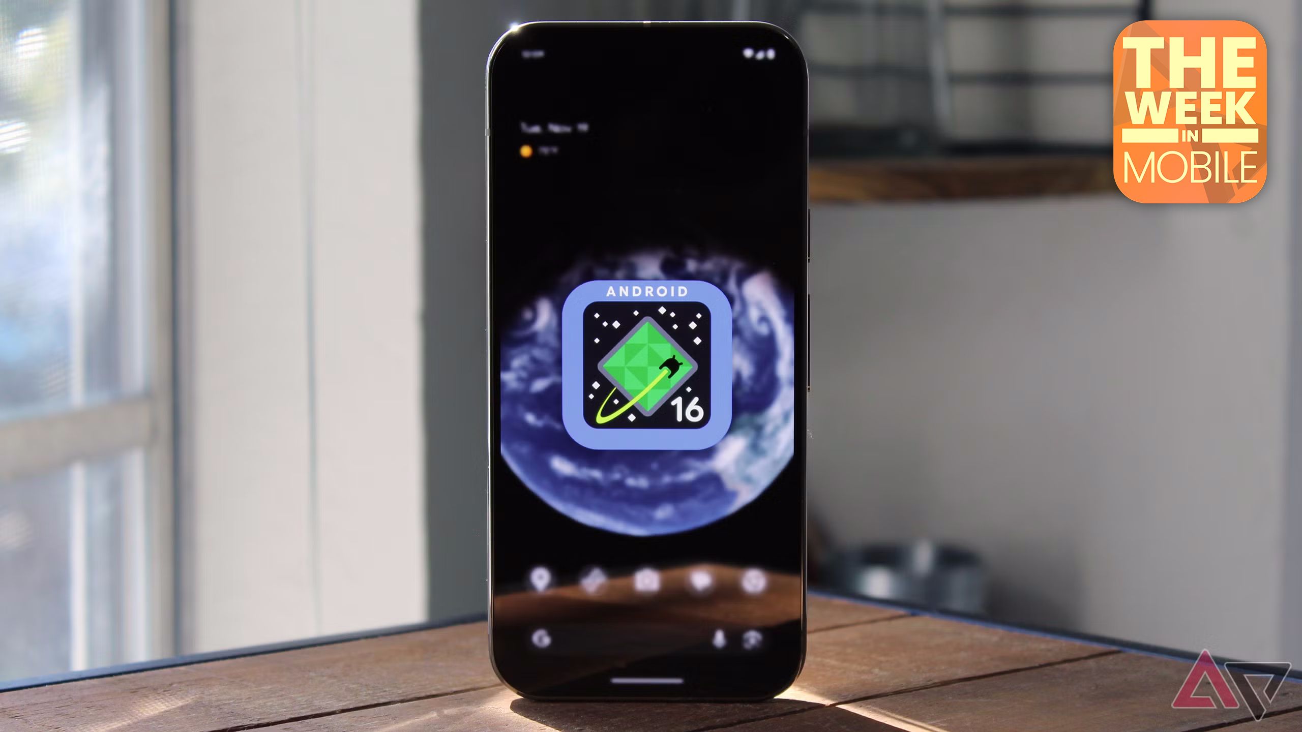 Image of the Android 16 logo on a Pixel 9 Pro's home screen with the phone sitting atop a wooden table.