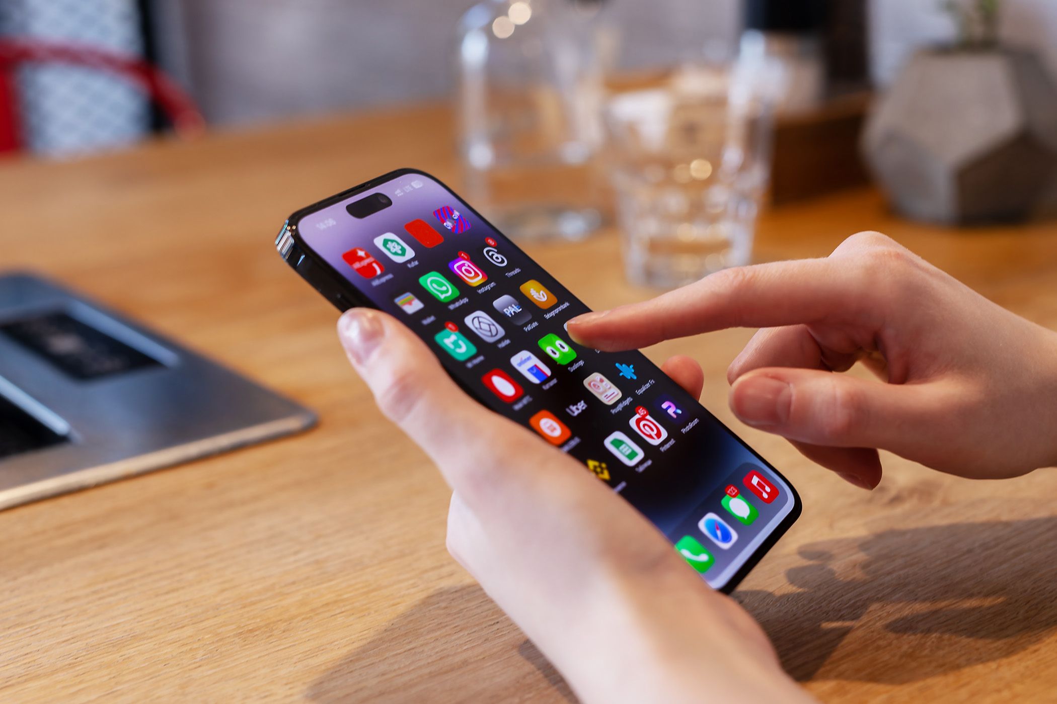 Person using an iphone at a table with a glass behind it.