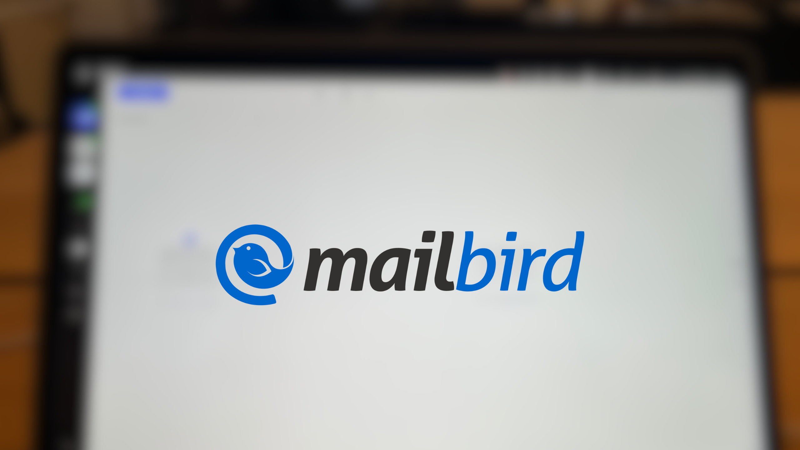 The Mailbird logo on top of a blurred image of a computer, which has the Mailbird app open