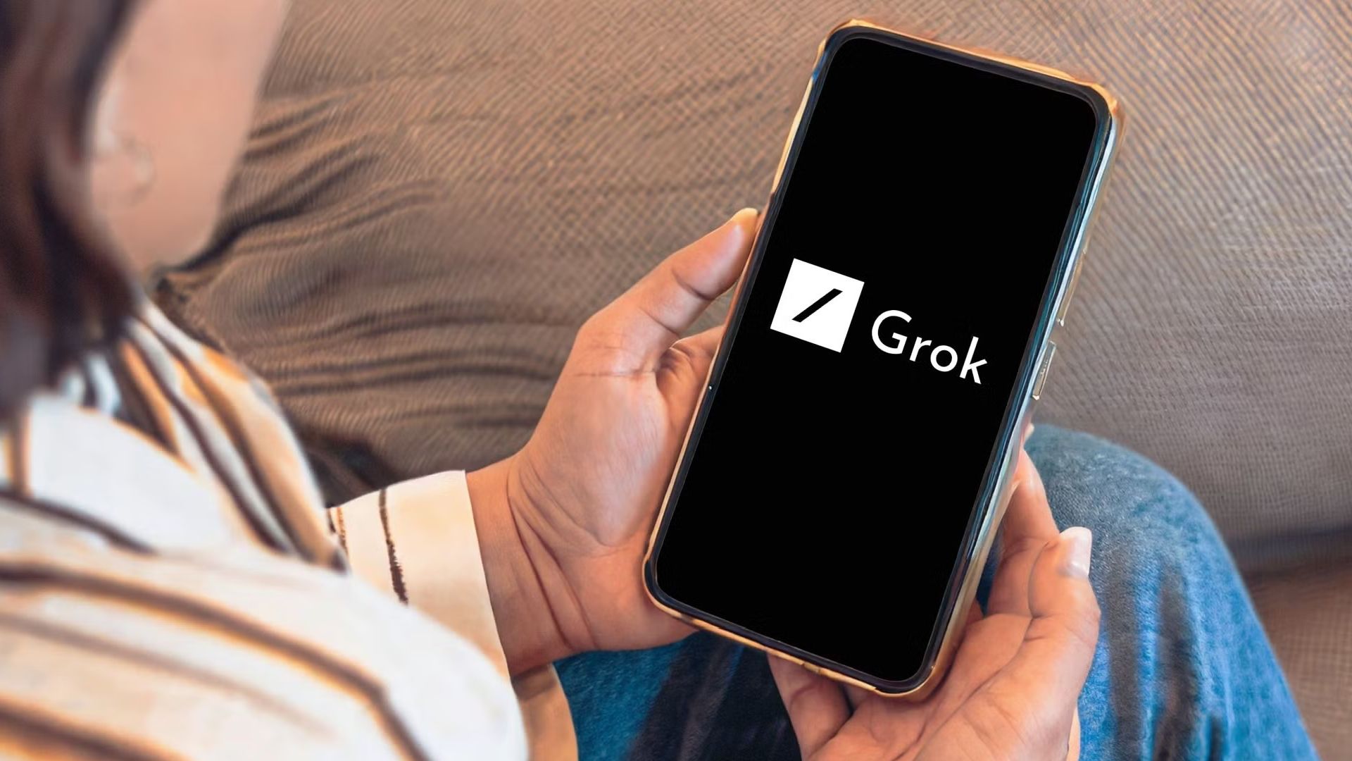 A person look at a smartphone with the grok logo. 