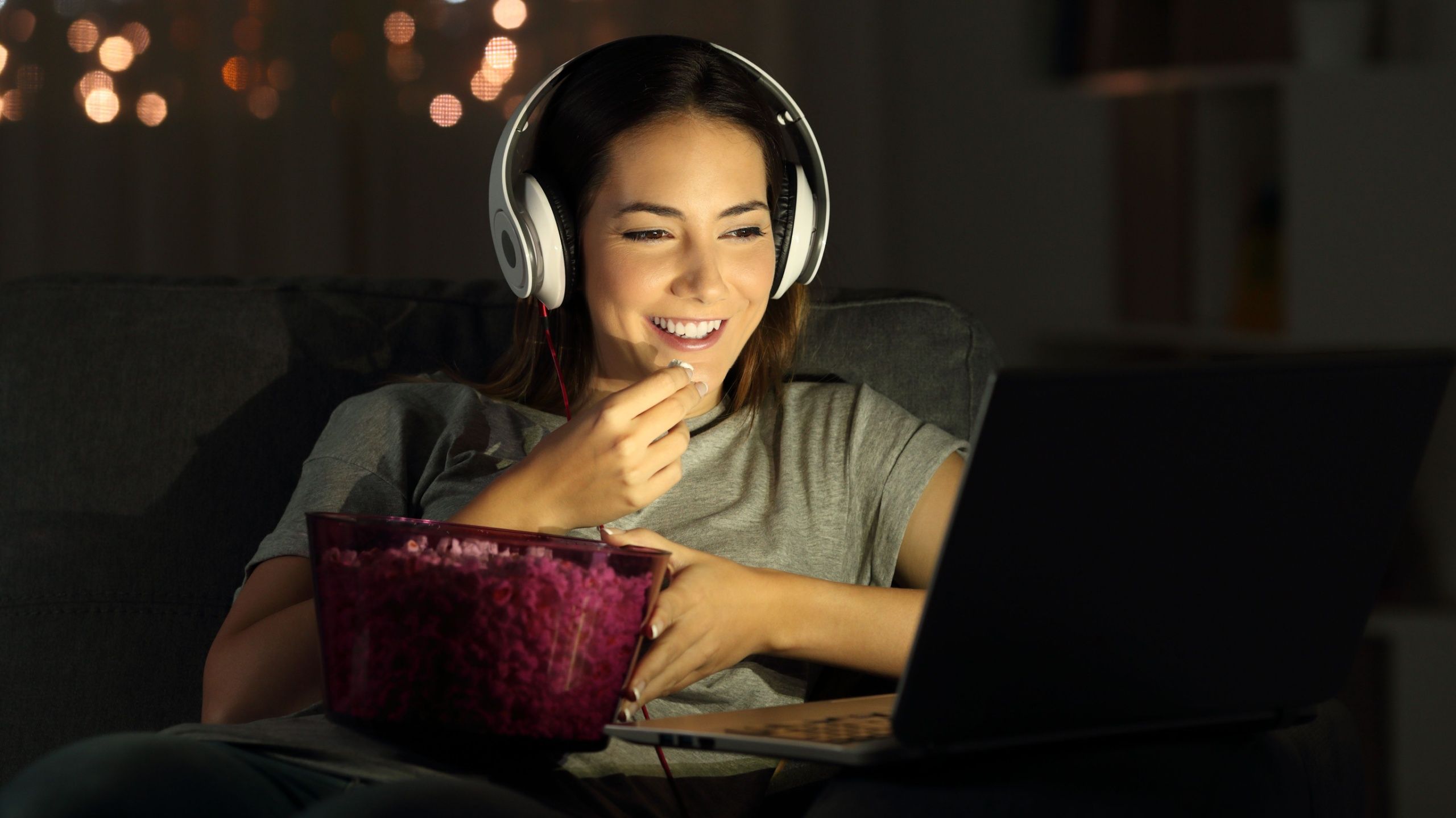 Woman watching movie on laptop with popcorn and headphones