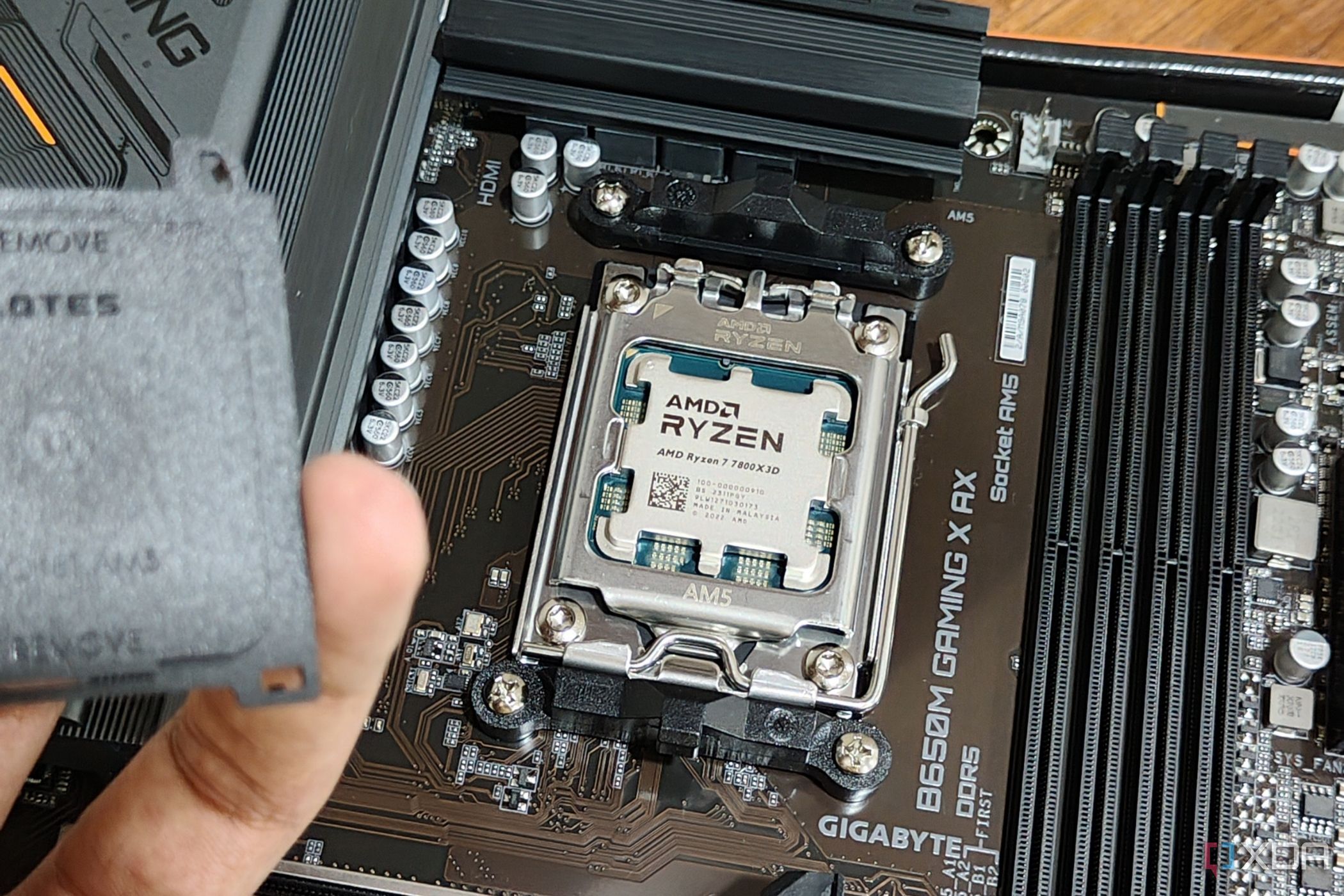 An image showing an AMD Ryzen 7 7800X3D CPU installed on a motherboard with a person in the foreground holding the socket cap in their hand.