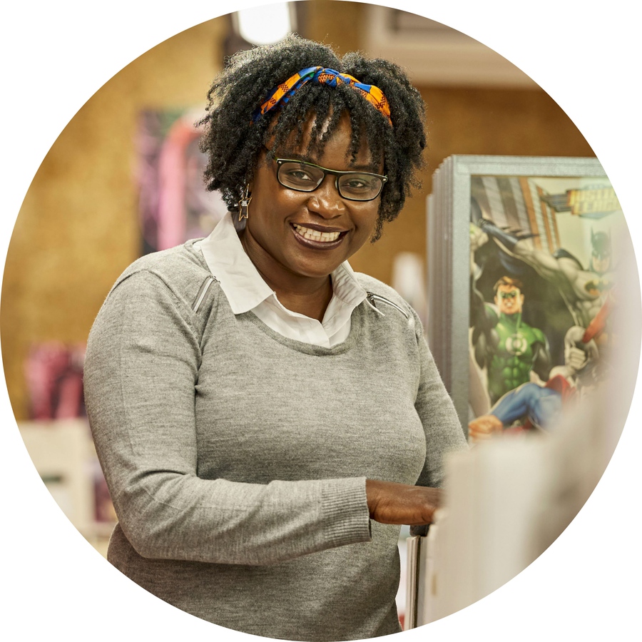 A bespectacled woman stands in the centre of a book and comic store, smiling.