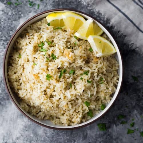 overhead shot of herb lemon rice in brown bowl with lemon slices