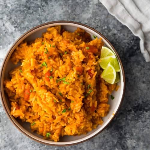 overhead shot of mexican rice with lime wedges in brown bowl on gray counter