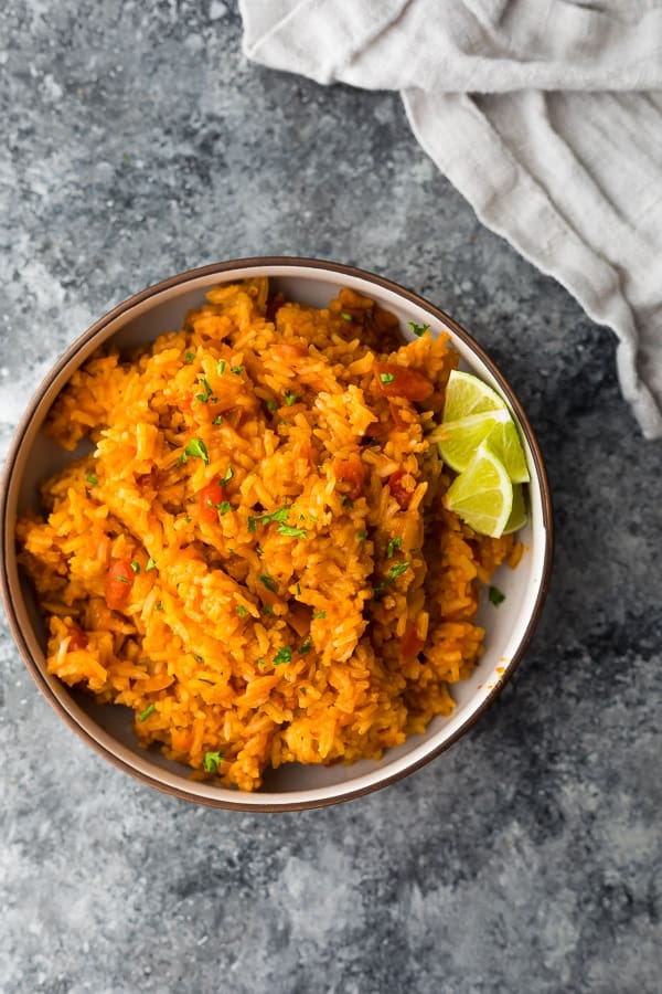 overhead shot of mexican rice with lime wedges in brown bowl on gray counter