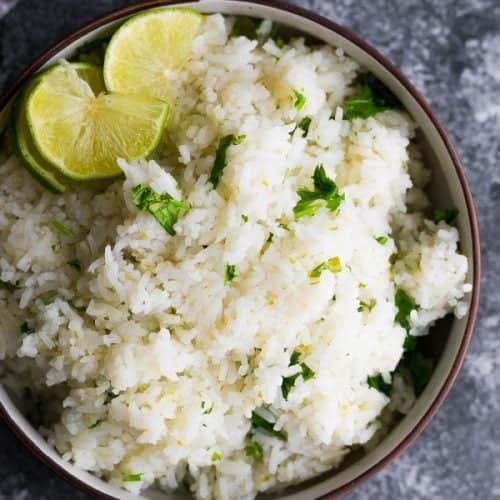 overhead shot of cilantro lime rice with lime wedge in brown bowl