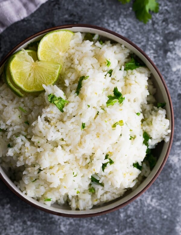 overhead shot of cilantro lime rice with lime wedge in brown bowl