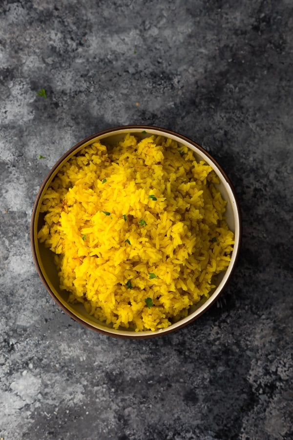 overhead shot of turmeric yellow rice in bowl on gray background