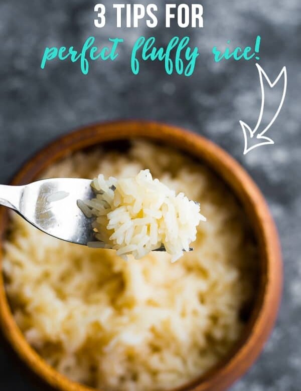 fork holding bite of white rice coming out of wood bowl