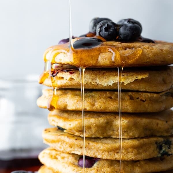 side image of stack of blueberry pancakes with syrup and fresh blueberries