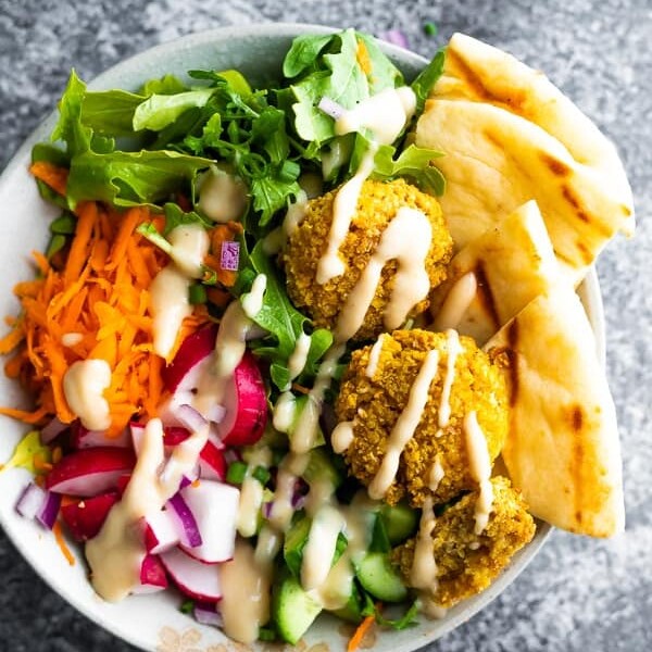 overhead shot of a falafel salad bowl with pita bread and dressing drizzled on top