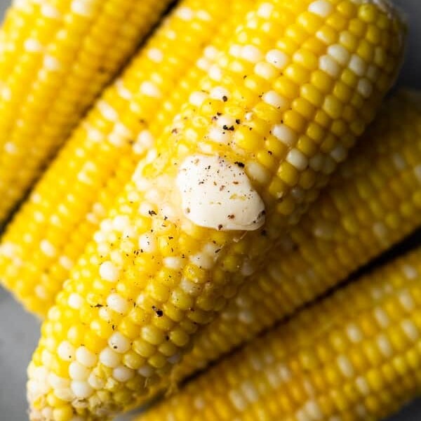 overhead shot of a pile of corn cobs with knob of butter and pepper on top