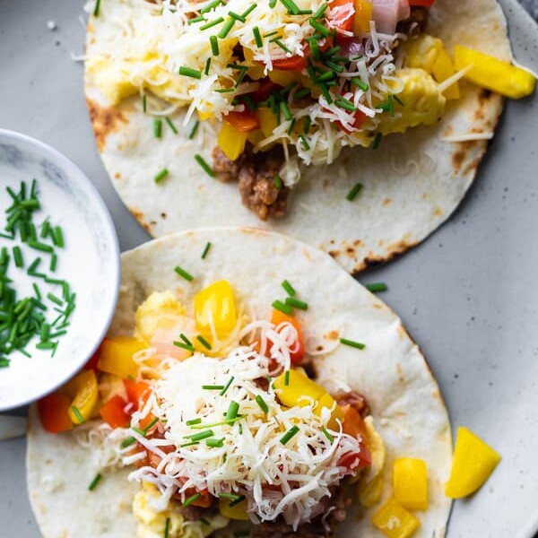 overhead shot of two breakfast tacos on a gray plate with side of sauce