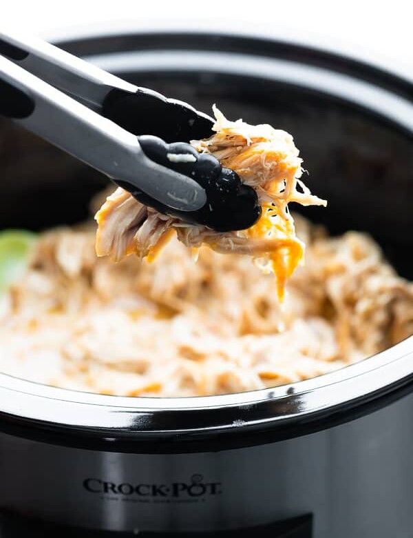 Honey lime chicken in the slow cooker with pair of tongs pulling some out