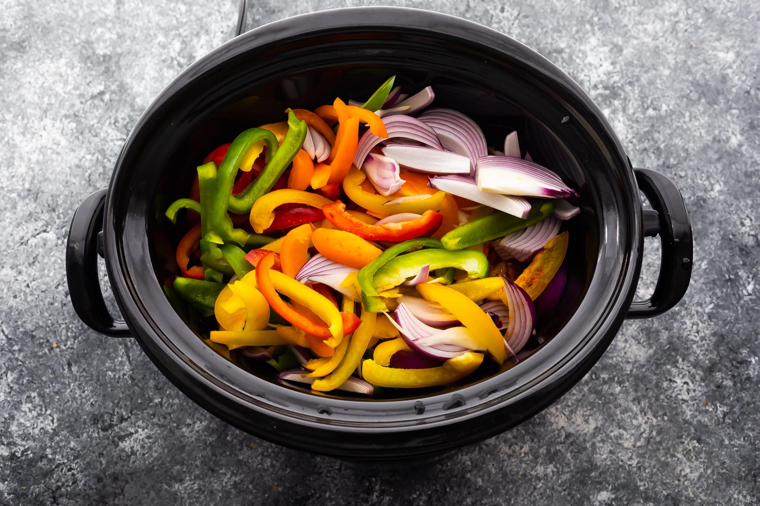 overhead view of slow cooker, bell peppers and onions added