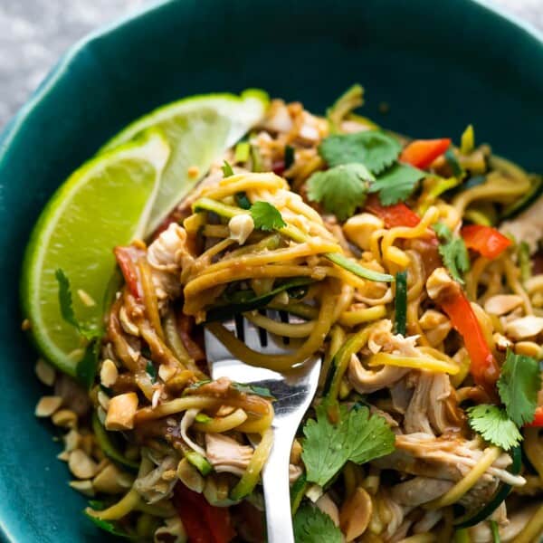 close up peanut chicken zucchini noodles in blue bowl with lime wedges