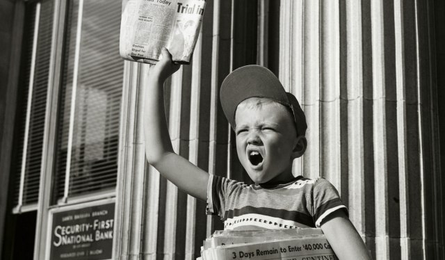 Boy selling newspapers in front of a building