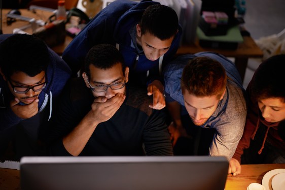 Shot of a group of shocked-looking young man staring at a monitor in a dark room