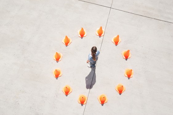 Person standing in a circle of traffic cones to represent rules, regulation, protection.