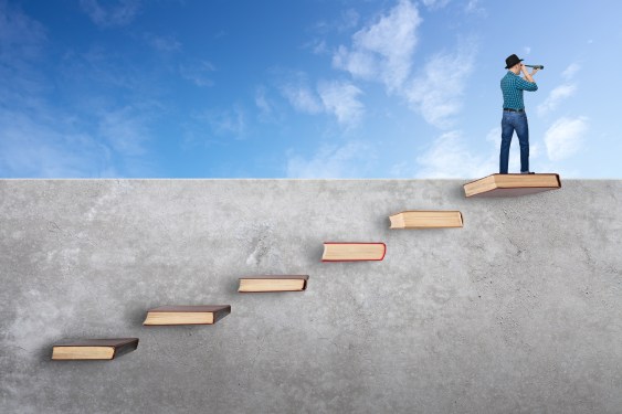 Man on top of wall with books like stairs. Looking through telescope