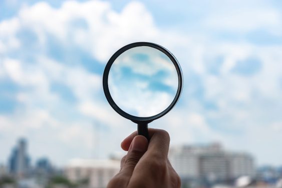 Hand holding a magnifying glass against the sky to represent search engine default choices.